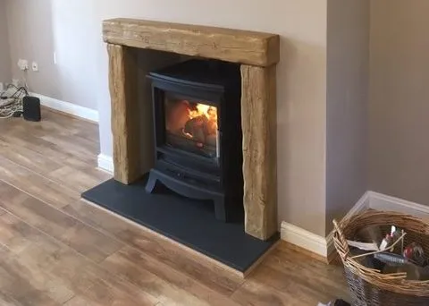 An attractive log burner with oak beam surround and black tiled hearth.